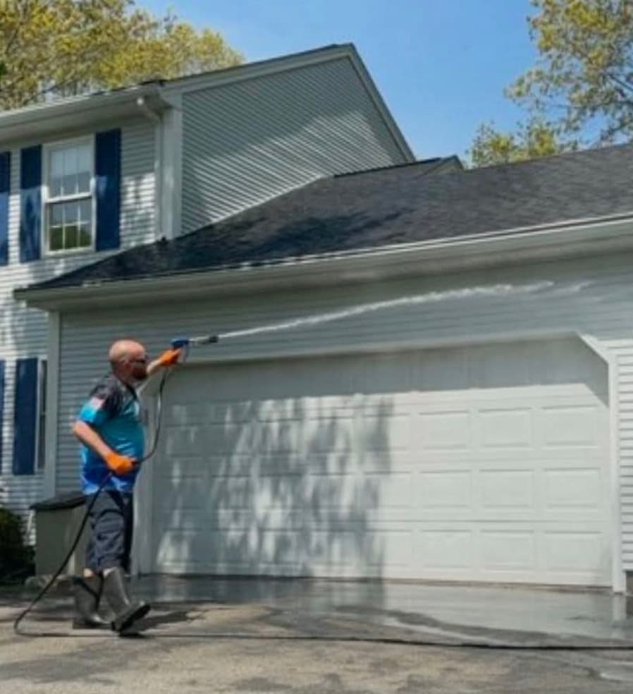 Technician pressure washing a garage door and siding on a two-story home